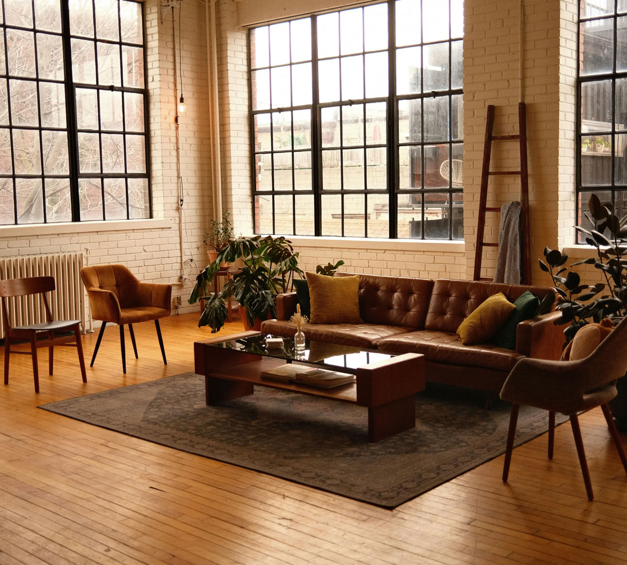Spacious loft-style living room with modern furniture, large windows, and warm lighting.